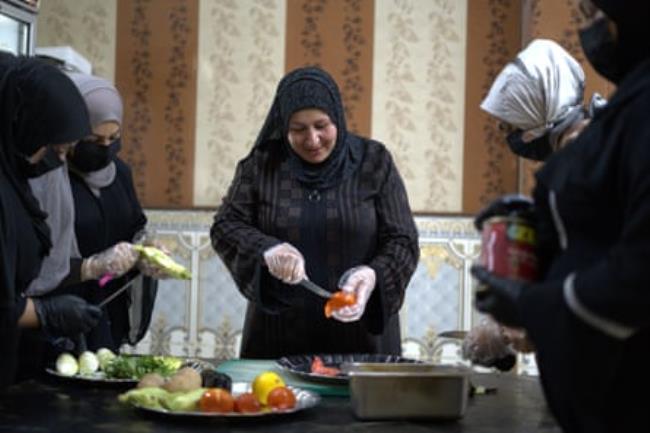 Women stand around a table wearing latex gloves to chop vegetables